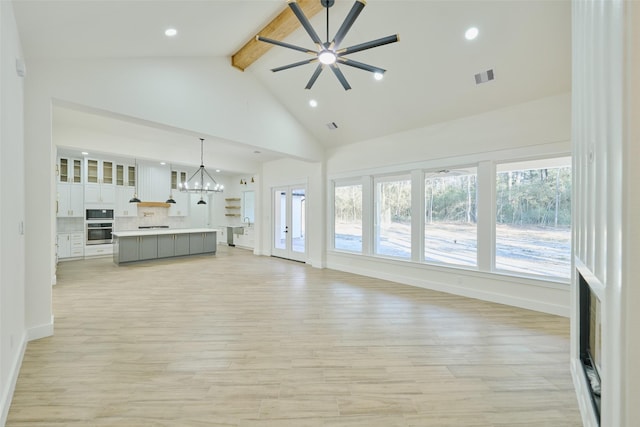 unfurnished living room with visible vents, light wood finished floors, high vaulted ceiling, beam ceiling, and ceiling fan with notable chandelier