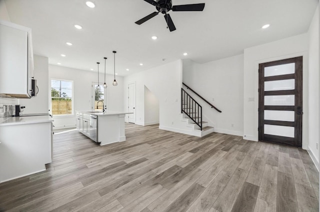 kitchen featuring white cabinetry, hanging light fixtures, a kitchen island with sink, and light wood-type flooring