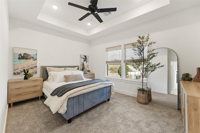 carpeted bedroom with a raised ceiling and ceiling fan