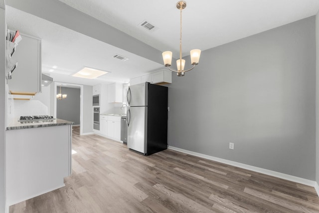 kitchen with appliances with stainless steel finishes, pendant lighting, hardwood / wood-style floors, white cabinetry, and a notable chandelier