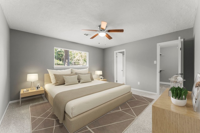 carpeted bedroom with ceiling fan, a textured ceiling, and a walk in closet