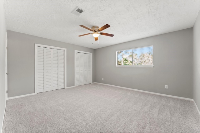 unfurnished bedroom with multiple closets, ceiling fan, carpet, and a textured ceiling