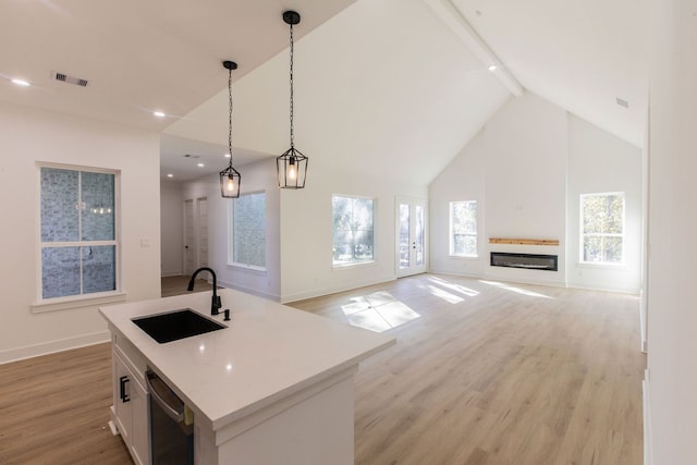 kitchen featuring white cabinetry, sink, decorative light fixtures, and an island with sink