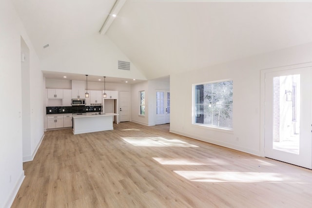 unfurnished living room with sink, a wealth of natural light, light hardwood / wood-style floors, and beamed ceiling