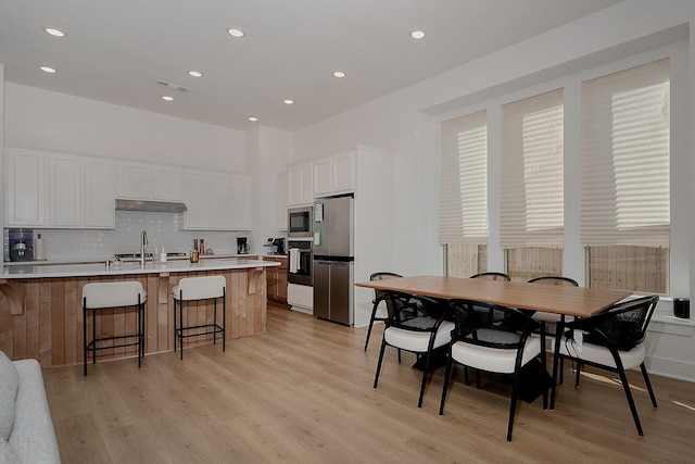 kitchen featuring stainless steel refrigerator, a kitchen breakfast bar, wall oven, white cabinets, and light wood-type flooring