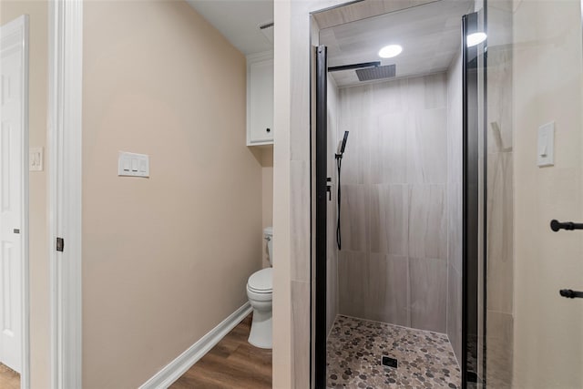 bathroom with toilet, a shower with door, and hardwood / wood-style floors