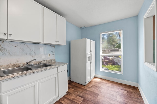 kitchen featuring white cabinetry, white refrigerator with ice dispenser, sink, and backsplash