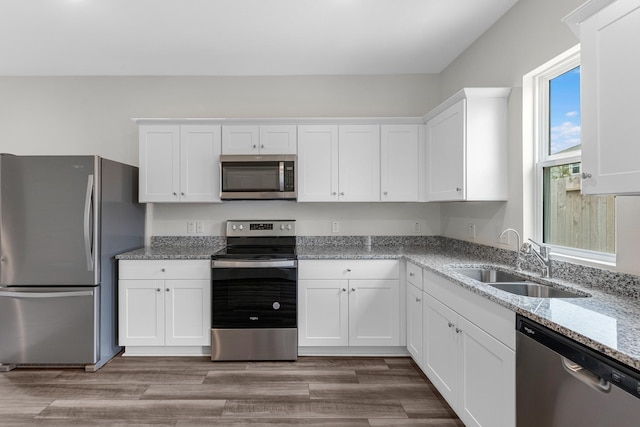 kitchen with white cabinetry, appliances with stainless steel finishes, light stone countertops, and sink