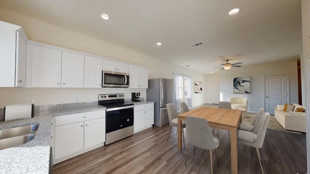 kitchen with appliances with stainless steel finishes, white cabinetry, ceiling fan, light stone counters, and light hardwood / wood-style floors