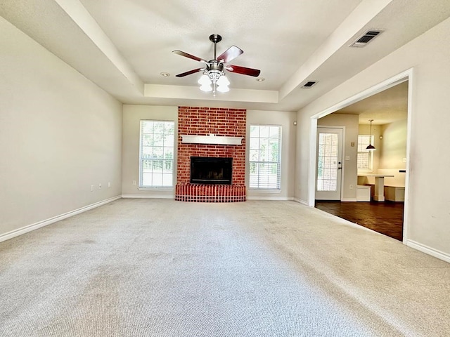 unfurnished living room featuring a brick fireplace, plenty of natural light, and a tray ceiling