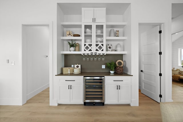 bar featuring white cabinets, built in features, beverage cooler, and light hardwood / wood-style flooring