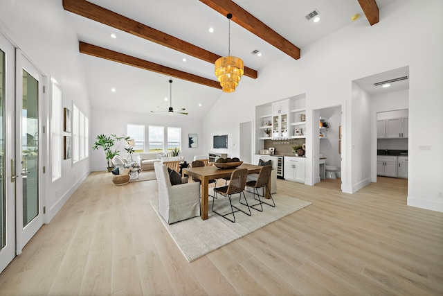 dining room with beam ceiling, a towering ceiling, built in features, and light wood-type flooring