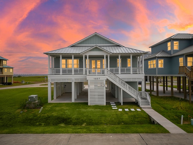 back house at dusk with a carport, a yard, central AC unit, a sunroom, and covered porch