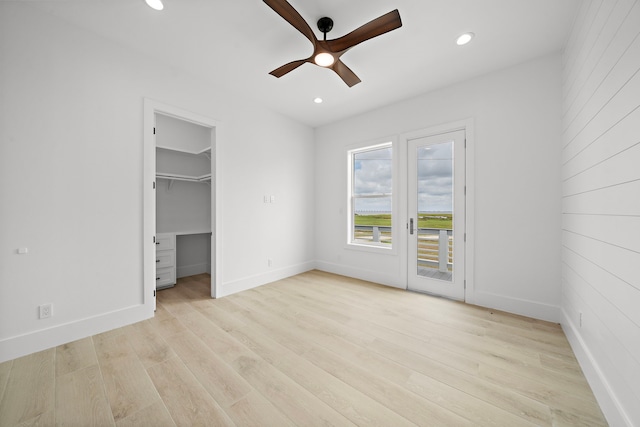 unfurnished bedroom with a spacious closet, access to exterior, light hardwood / wood-style floors, ceiling fan, and a closet