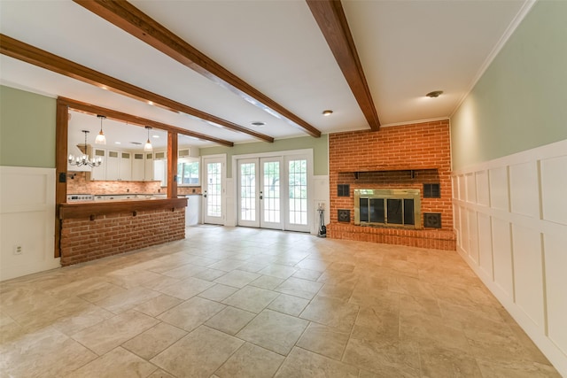 unfurnished living room with beam ceiling, ornamental molding, a brick fireplace, french doors, and a chandelier