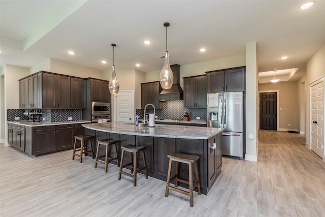 kitchen featuring appliances with stainless steel finishes, a breakfast bar, pendant lighting, dark brown cabinets, and a center island with sink