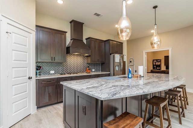 kitchen featuring appliances with stainless steel finishes, hanging light fixtures, dark brown cabinets, custom range hood, and a spacious island