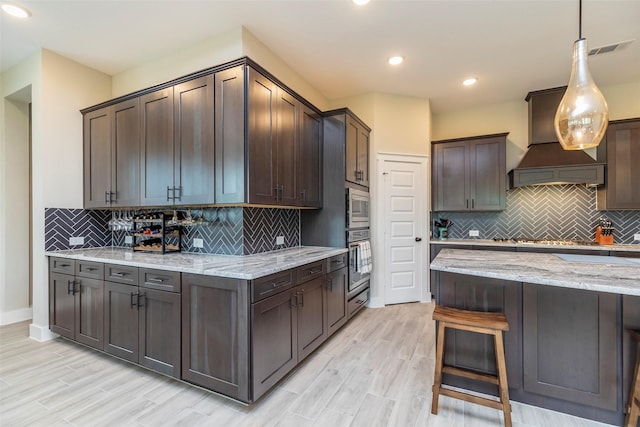 kitchen featuring stainless steel appliances, light stone countertops, hanging light fixtures, and dark brown cabinetry