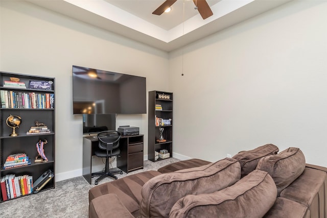 office space with light carpet, a tray ceiling, and ceiling fan