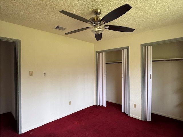 unfurnished bedroom featuring dark carpet, multiple closets, a textured ceiling, and ceiling fan