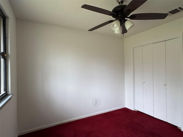 unfurnished bedroom featuring dark colored carpet, a textured ceiling, ceiling fan, and a closet