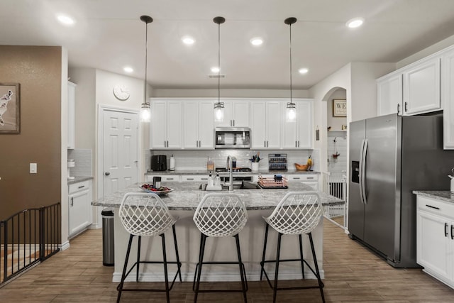 kitchen featuring white cabinetry, pendant lighting, stainless steel appliances, light stone countertops, and a kitchen island with sink