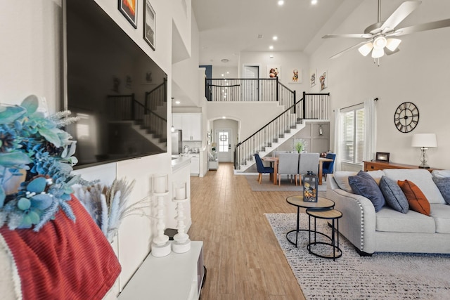 living room featuring a high ceiling, a wealth of natural light, ceiling fan, and light wood-type flooring