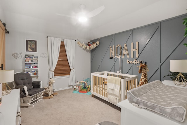 bedroom with a crib, a barn door, light carpet, and ceiling fan