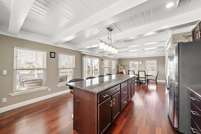 kitchen featuring pendant lighting, stainless steel refrigerator, beam ceiling, light stone counters, and a kitchen island