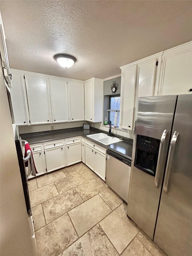 kitchen with dark countertops, appliances with stainless steel finishes, white cabinetry, a sink, and a textured ceiling