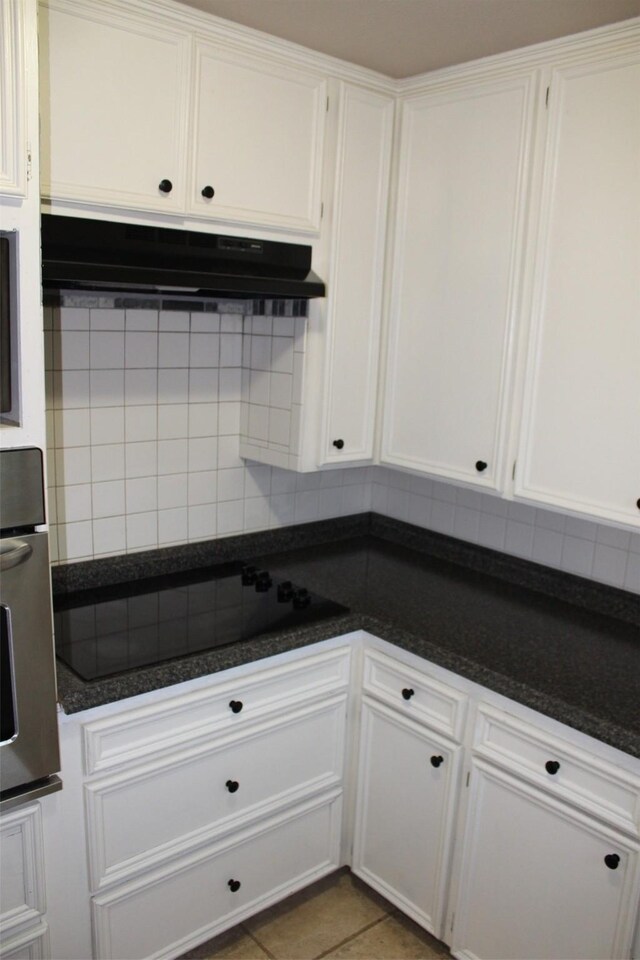 kitchen with decorative backsplash, oven, tile patterned flooring, black electric stovetop, and under cabinet range hood