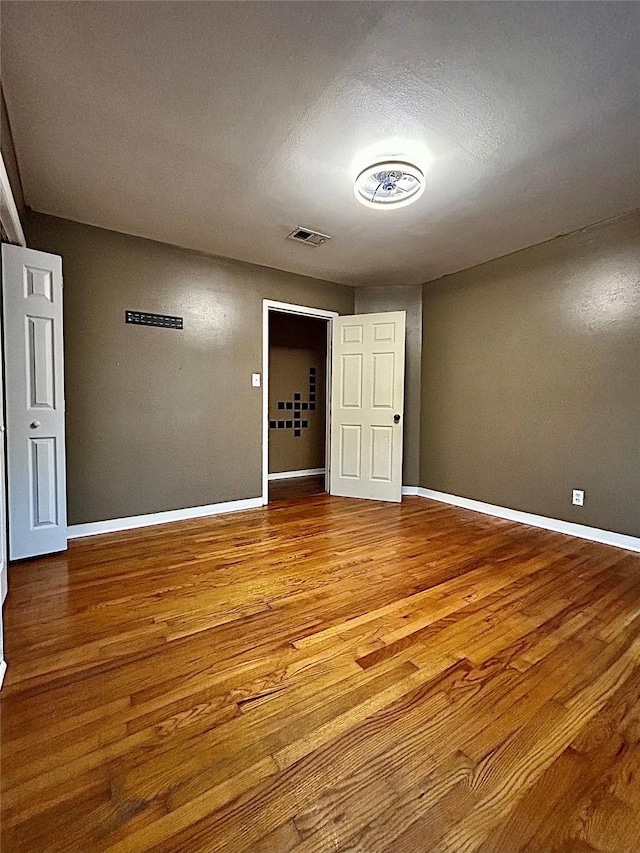 unfurnished room featuring wood finished floors, visible vents, and baseboards