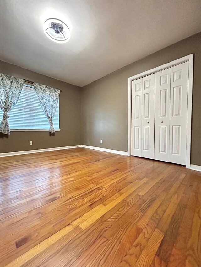 unfurnished bedroom featuring a closet, wood finished floors, and baseboards