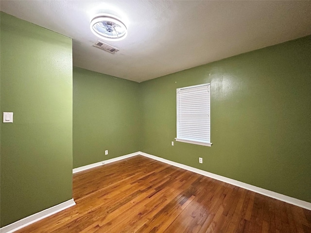 spare room with baseboards, visible vents, and wood finished floors