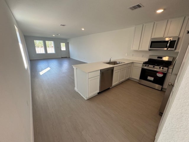 kitchen with sink, light wood-type flooring, appliances with stainless steel finishes, kitchen peninsula, and white cabinets