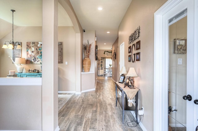 hallway with arched walkways, recessed lighting, an inviting chandelier, wood finished floors, and baseboards