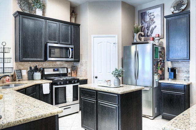 kitchen featuring appliances with stainless steel finishes, dark cabinetry, a sink, and backsplash