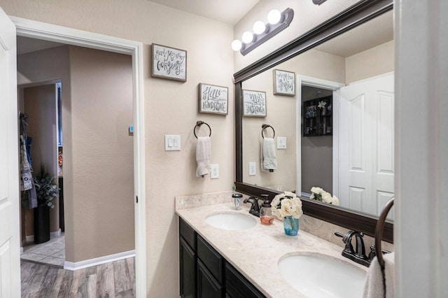 full bath featuring double vanity, wood finished floors, a sink, and baseboards