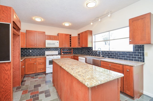 kitchen with sink, white appliances, a center island, light stone countertops, and a textured ceiling