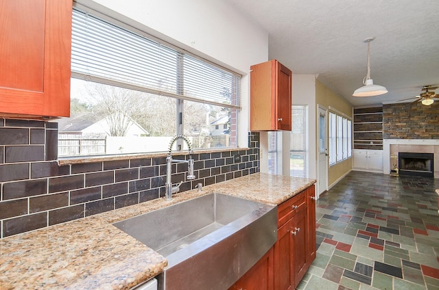 kitchen featuring sink, light stone counters, hanging light fixtures, a fireplace, and backsplash