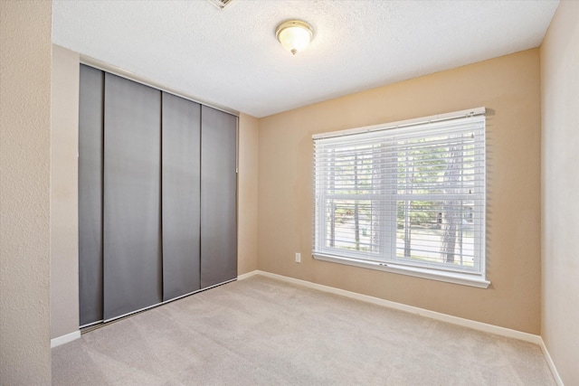 unfurnished bedroom with a closet, light carpet, and a textured ceiling