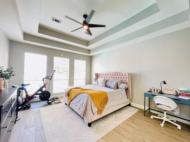 bedroom featuring ceiling fan, a raised ceiling, and light wood-type flooring