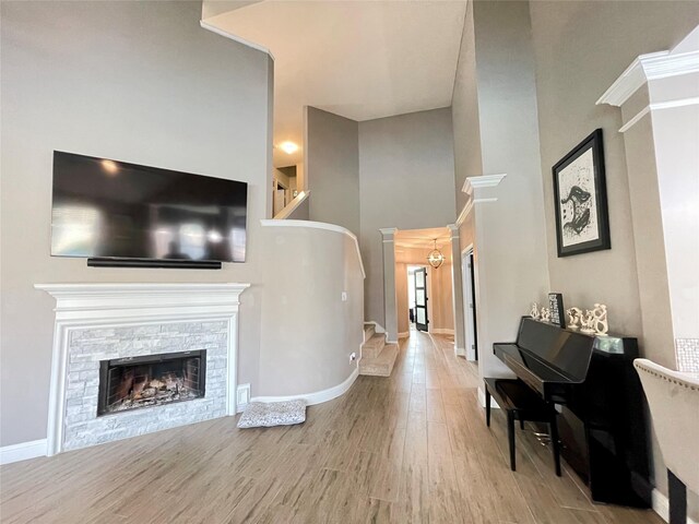 living room with a stone fireplace, light hardwood / wood-style floors, decorative columns, and a high ceiling