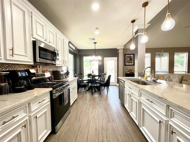 kitchen featuring sink, light stone counters, decorative light fixtures, appliances with stainless steel finishes, and white cabinets