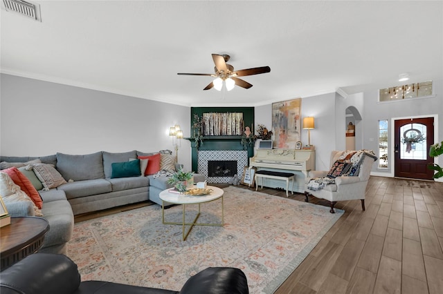 living room featuring ceiling fan, wood-type flooring, a tiled fireplace, and ornamental molding