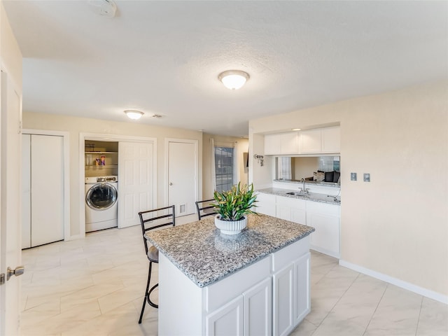 kitchen featuring a kitchen island, stone countertops, washer / clothes dryer, sink, and white cabinets