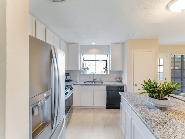 kitchen with appliances with stainless steel finishes, sink, white cabinets, light stone counters, and a textured ceiling