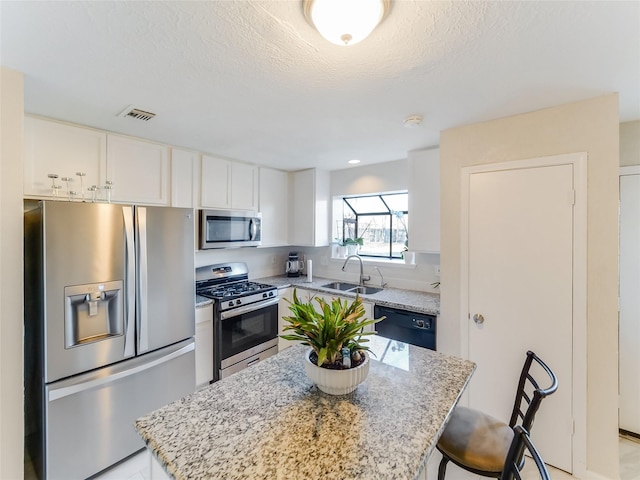 kitchen featuring sink, a center island, stainless steel appliances, light stone countertops, and white cabinets