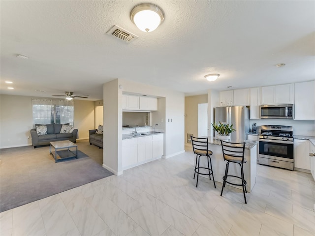 kitchen with a textured ceiling, stainless steel appliances, a kitchen breakfast bar, and white cabinets