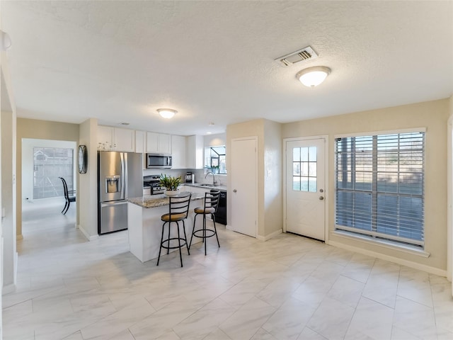 kitchen featuring appliances with stainless steel finishes, white cabinets, a kitchen breakfast bar, a center island, and light stone counters